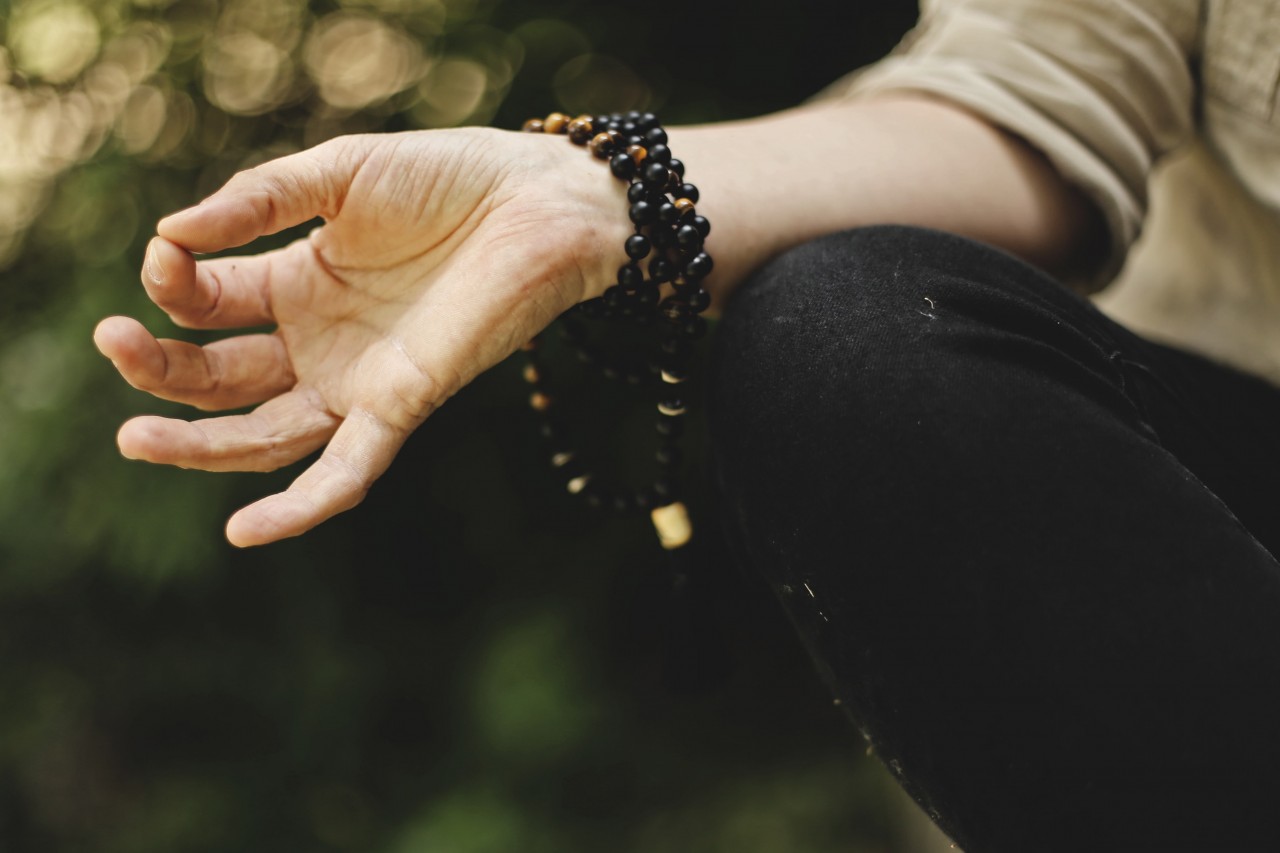 close up of a woman's hand in a mudra position with mala beads wrapped around her wrist